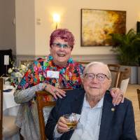 Don Lubbers sitting and Bari Johnson standing behind him, both smiling for camera